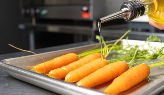 Pouring cottonseed oil on carrots on a baking sheet